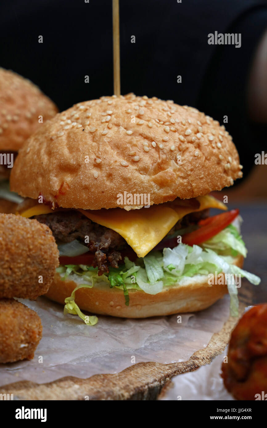 Big American Cheeseburger mit gezogenes Schweinefleisch und Salat in Sesam Brötchen auf Pergament Papier über natürliche Holz geschnitten, Nahaufnahme, niedrigen Winkel Ansicht Stockfoto