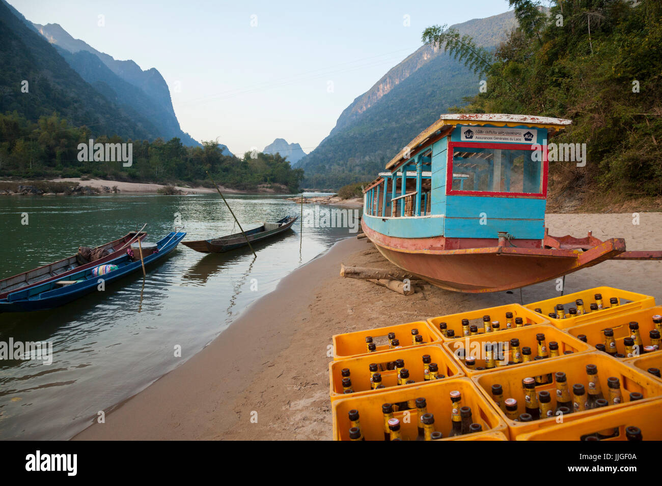 Boote und einen großen Stapel von leeren Beer Lao (nationales Bier) am Ufer des Flusses Nam Ou in Muang Ngoi, Laos. Das Bier ist notwendige Brennmaterial für den lebendigen Tourismus rund um die Stadt zentriert. Stockfoto