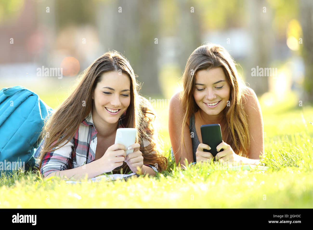 Vorderansicht von zwei Studenten SMS in ihren Smartphones liegen auf dem Rasen in einem park Stockfoto