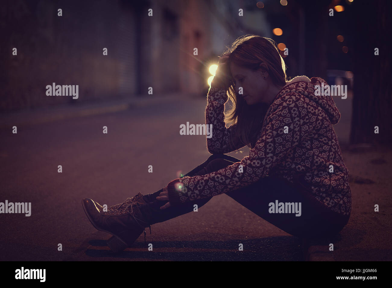 Frau sitzt auf dem Bürgersteig in der Nacht Stockfoto