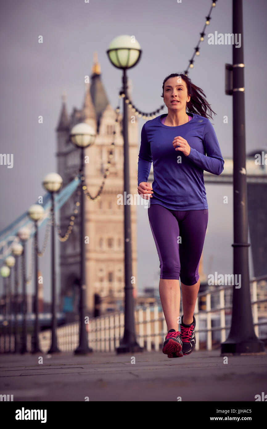 Eine Frau, die neben der Themse mit Tower Bridge im Hintergrund laufen. Stockfoto