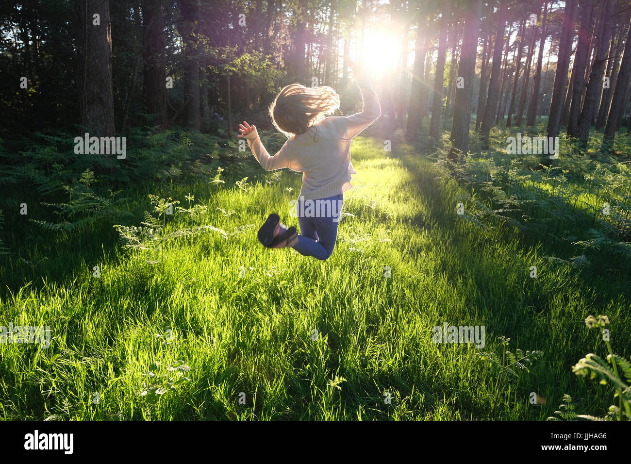 Ein junges Mädchen springen vor Freude in einem sonnendurchfluteten Wald. Stockfoto