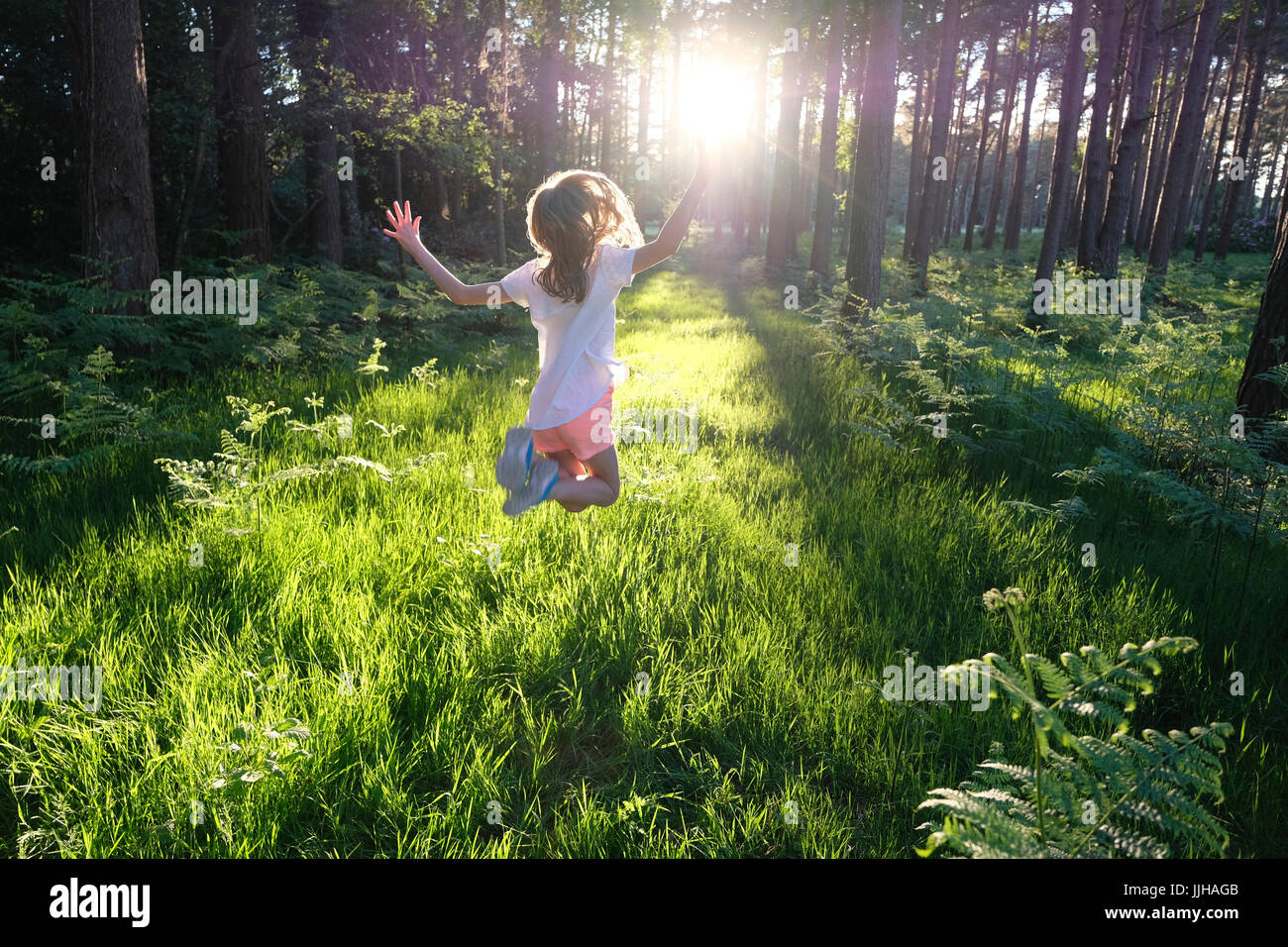 Ein junges Mädchen springen vor Freude in einem sonnendurchfluteten Wald. Stockfoto