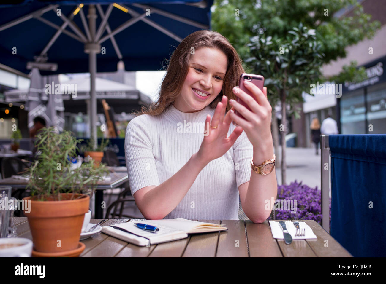 Eine junge Frau überprüft ihr Handy außerhalb in einem Café sitzen. Stockfoto