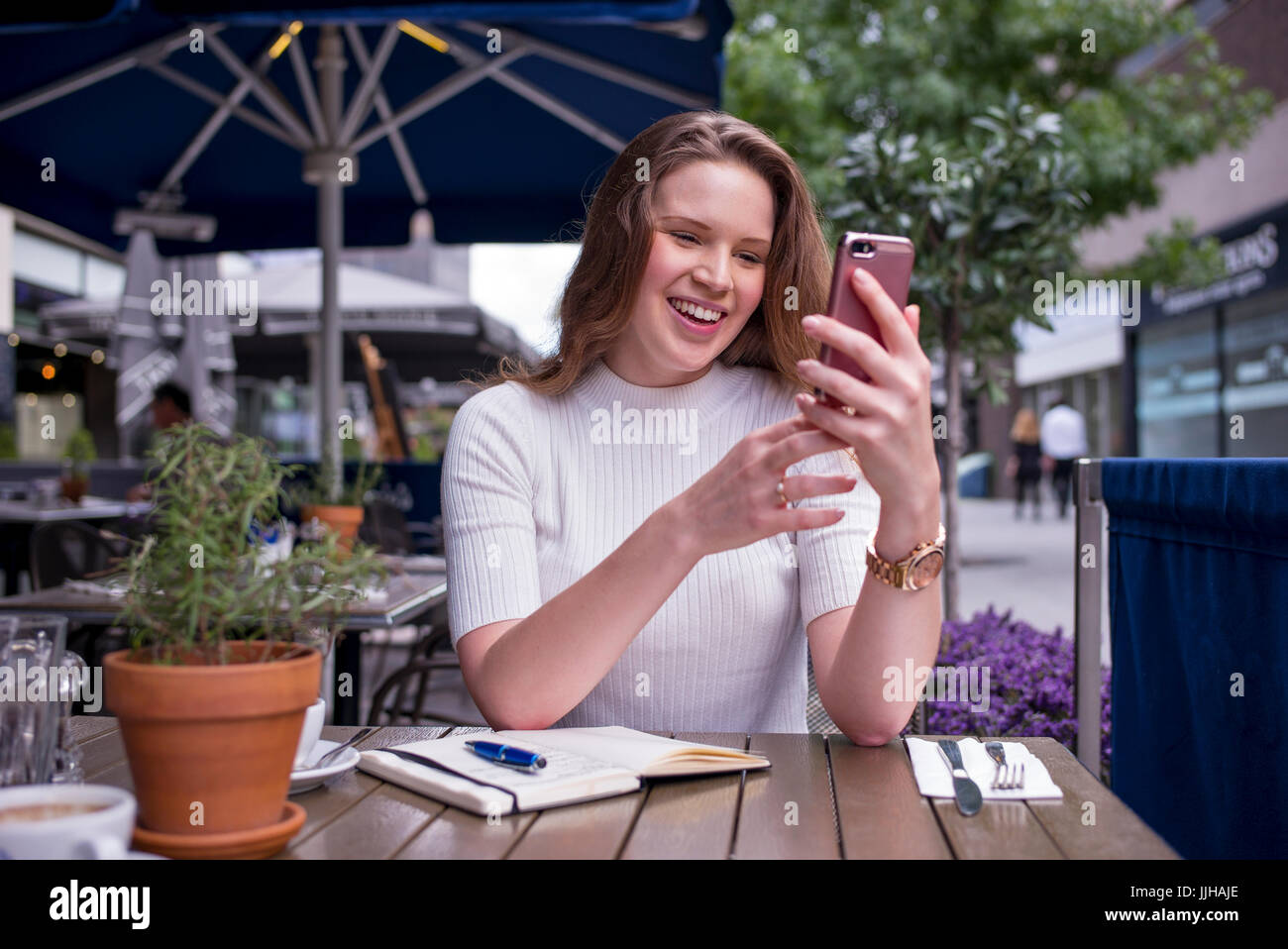 Eine junge Frau überprüft ihr Handy außerhalb in einem Café sitzen. Stockfoto
