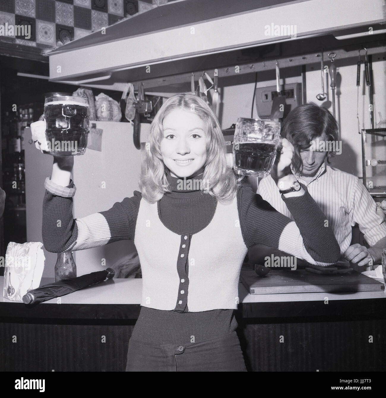 1970er Jahre, England, Rag Woche feiern, hält eine junge blonde Schülerin trug ein Tank-Top zwei Pints Bitter. Stockfoto