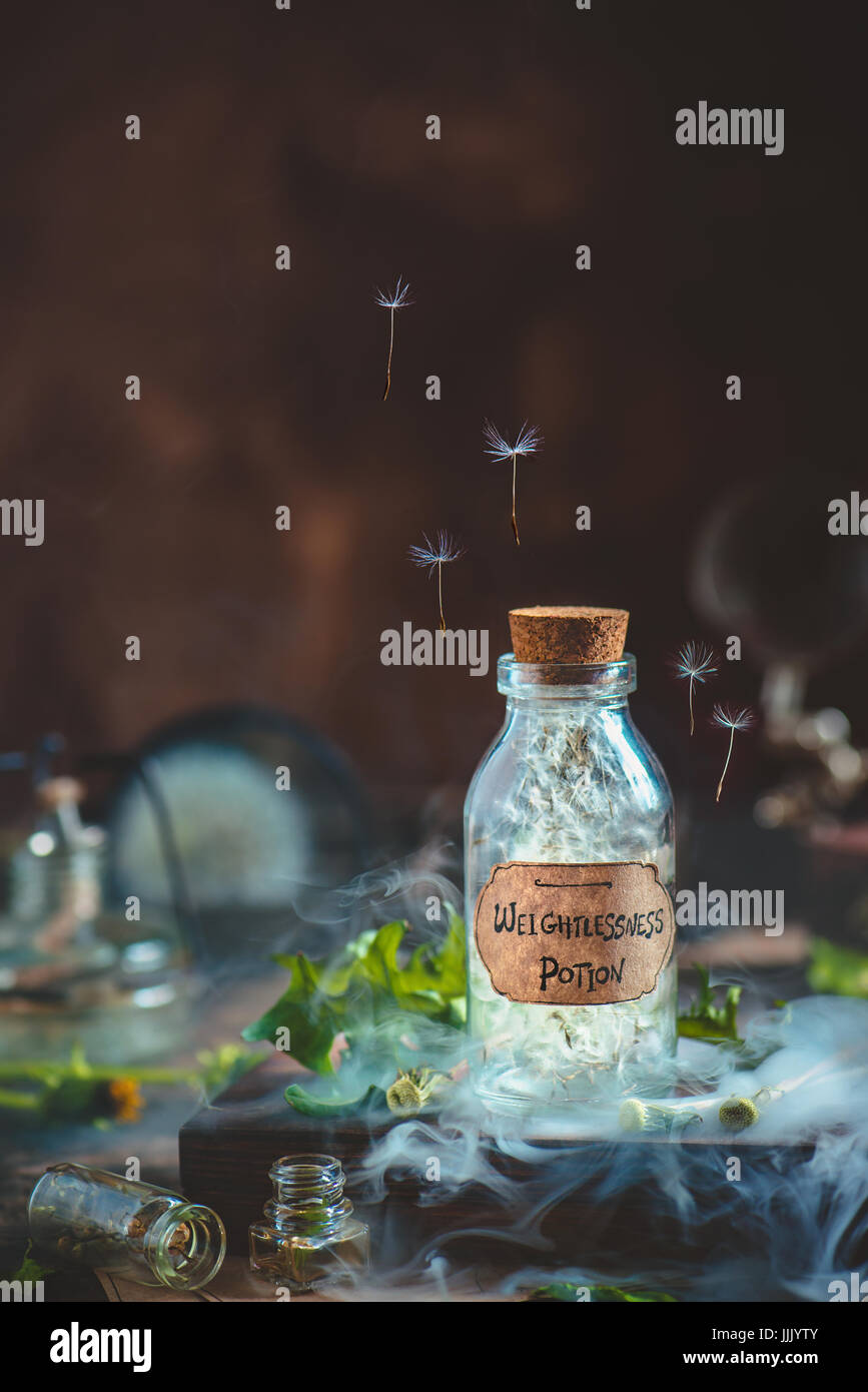 Trank Glasflasche mit Löwenzahnsamen und handgefertigten Label in eine magische Stillleben mit Rauch und fliegende Samen Stockfoto