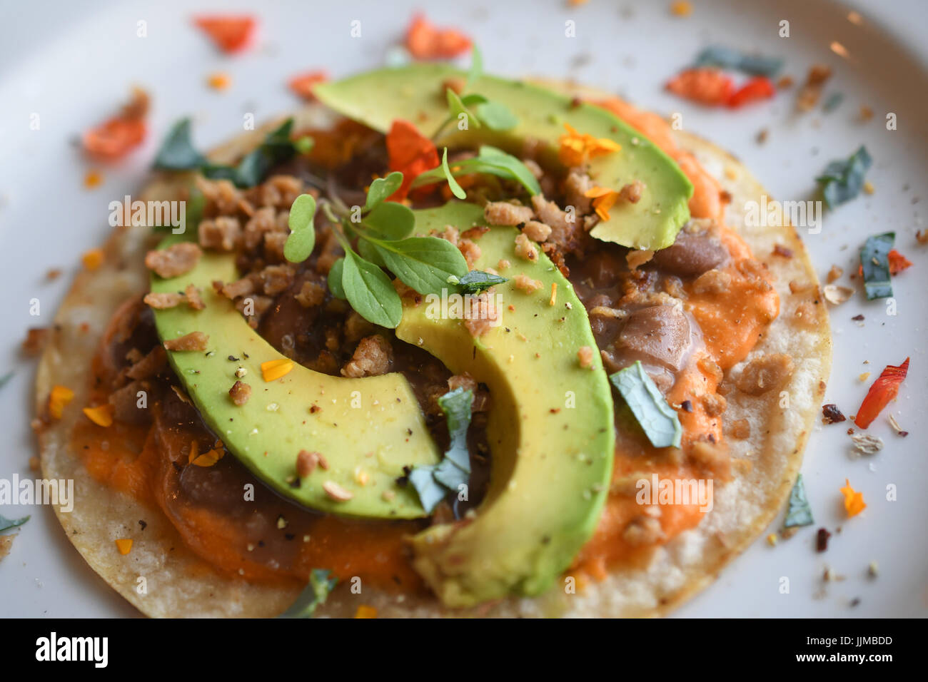 Taco Dienstag, vegane Tacos mit Chorizo-Bohnen, veganen Käse, Avocado, blaue Blume Blütenblatt und eine gelbe Blume. Stockfoto