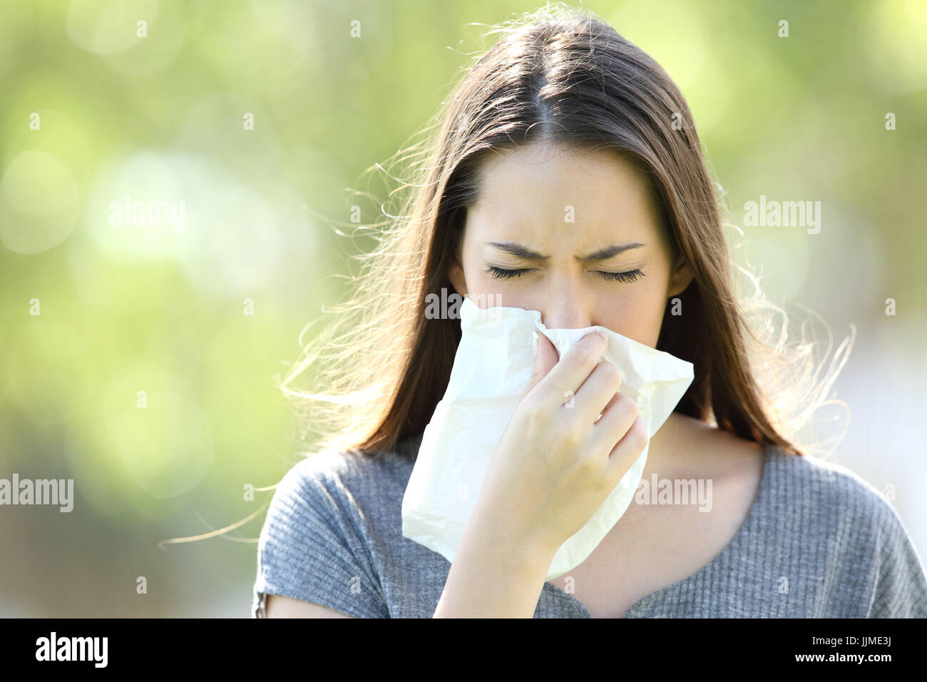 Vorderansicht eines einzigen Mädchens Niesen und bläst in ein Tuch im Freien mit einem grünen Hintergrund Stockfoto