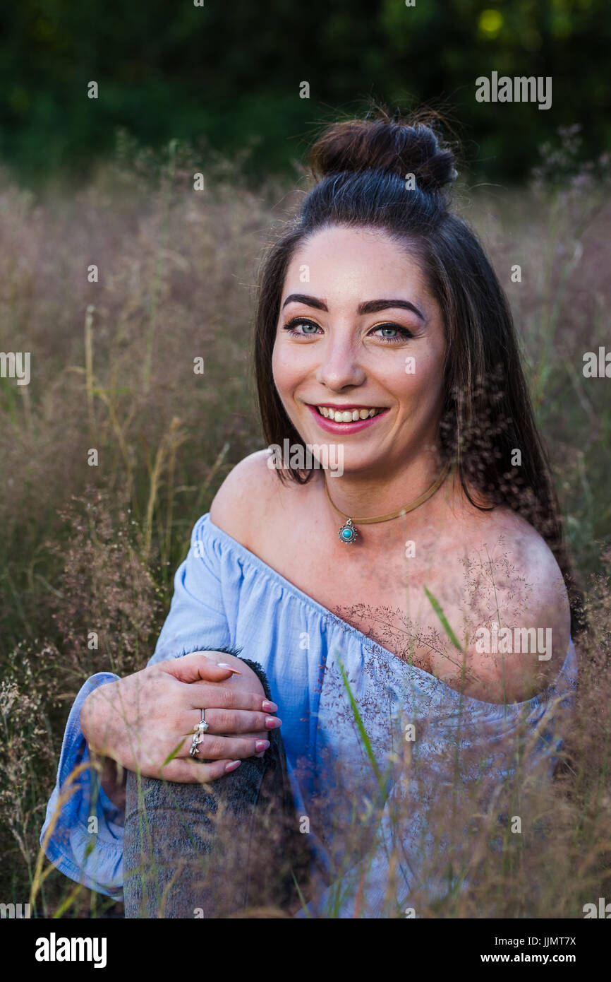 Eine wunderschöne junge Frau sitzt auf einer Wiese lange Gras in der Nähe von Liverpool eine Sommer Abend leichtes ziehen ihre Knie in Richtung Brust. Stockfoto