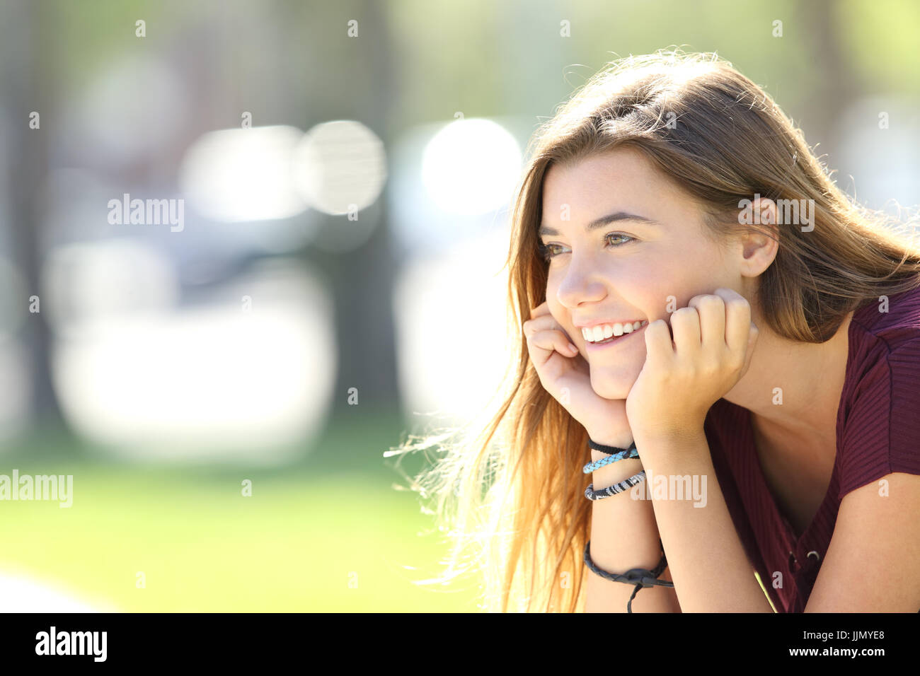 Porträt eines einzigen glücklich Teen Lächeln auf den Lippen und auf der Suche entfernt sitzt in einem park Stockfoto