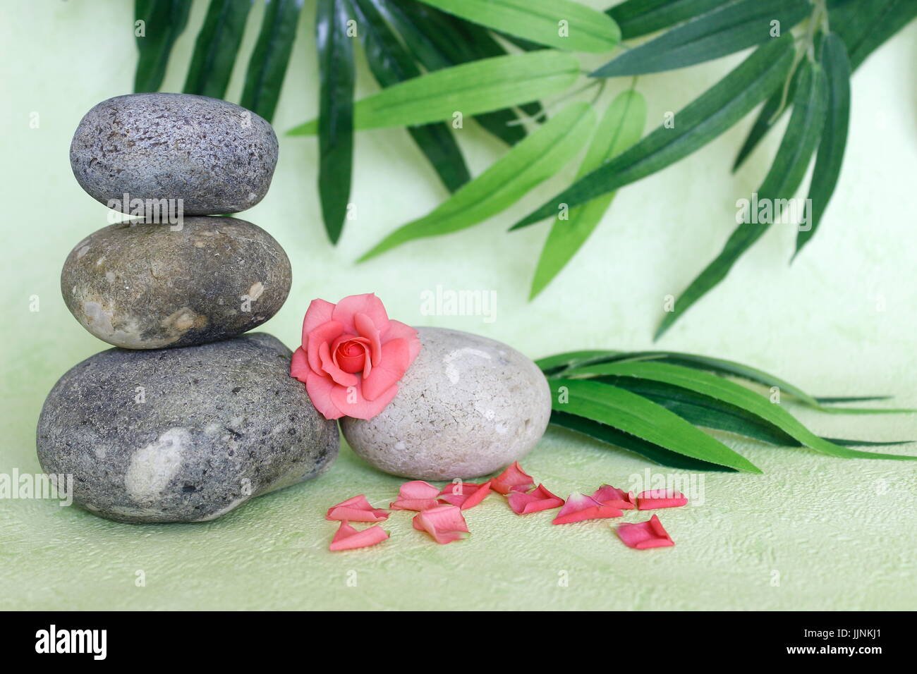 Dekorative Kieselsteine in Zen Leben Mode mit einer rosa Blume auf grün und Laub Hintergrund gestapelt Stockfoto