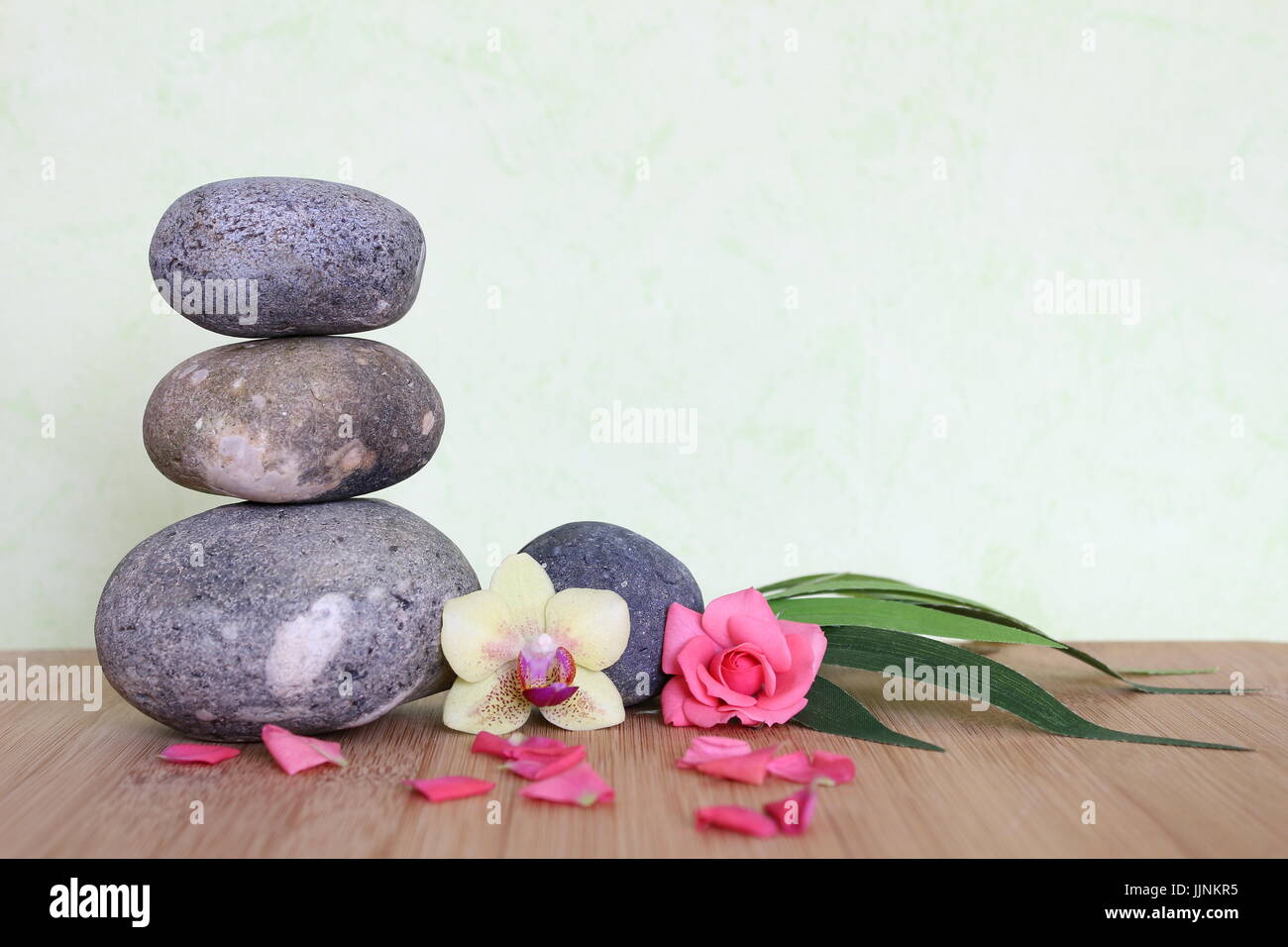 Dekorative Kieselsteine gestapelt in einem Zen Leben Mode auf einem Bambus-Holzbrett mit einer rosa Blume und einer Orchidee auf grünem Hintergrund Stockfoto