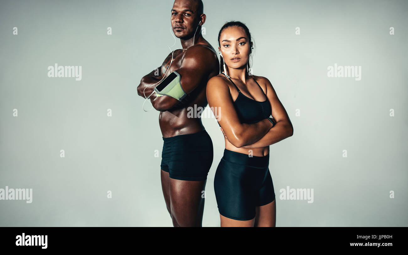 Porträt der schönen sportlichen paar zusammenstehen auf grauem Hintergrund. Muskulösen jungen Mann und Frau mit verschränkten Armen Blick in die Kamera. Stockfoto