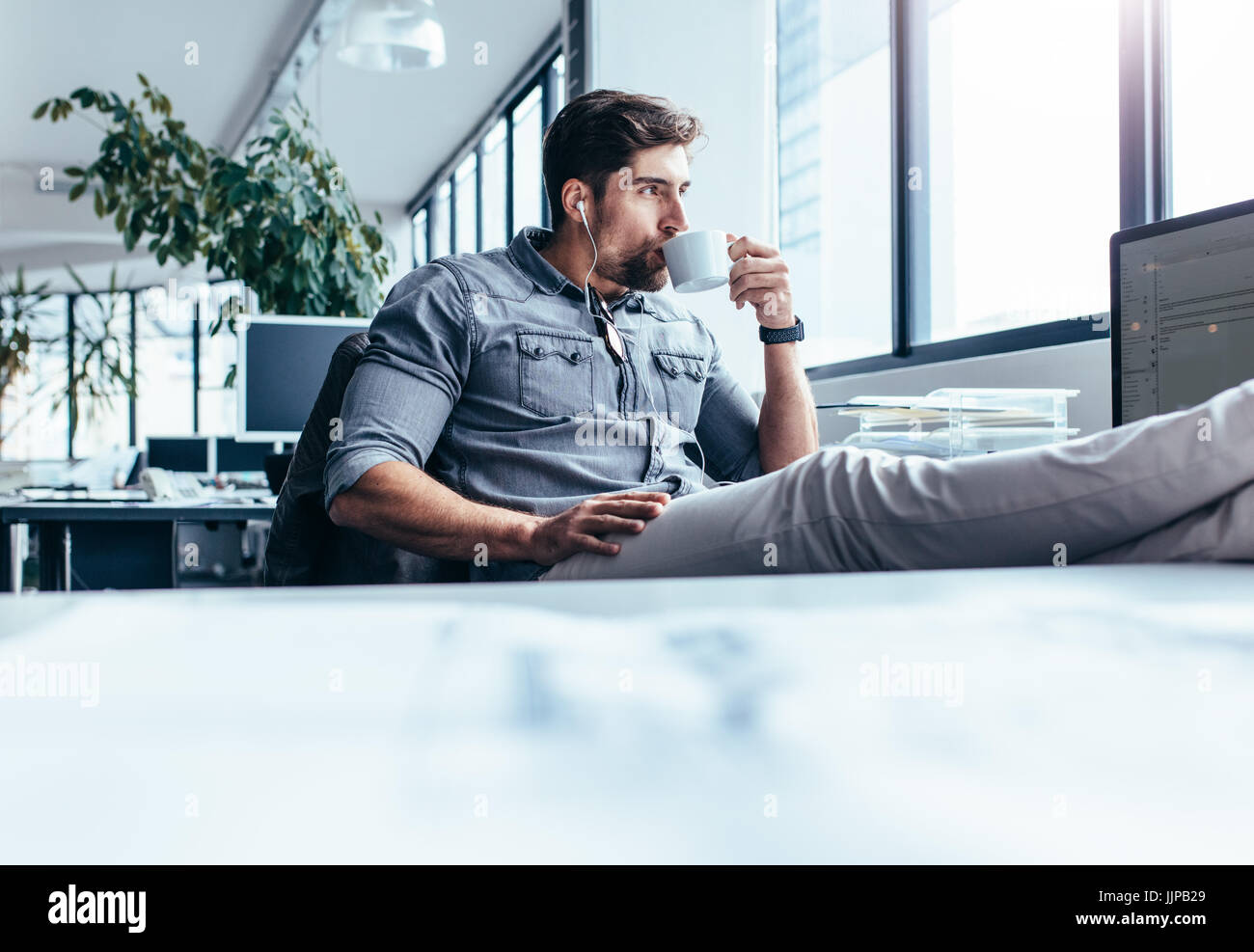 Junger Mann trinken Kaffee während der Pause im Büro. Geschäftsmann Musik hören mit Tasse Kaffee. Stockfoto Junger Mann trinken Kaffee während der Pause im Büro. Geschäftsmann Musik hören mit Tasse Kaffee. Stockfoto