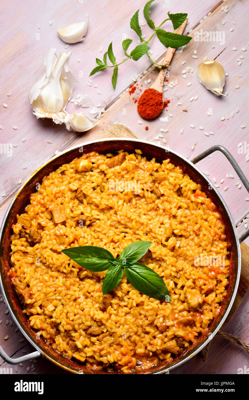 High-Angle Shot ein spanisches Huhn Paella in einem Paellera, Paella-Pfanne und einige Zutaten Zubereitung auf einem rustikalen Holztisch Stockfoto