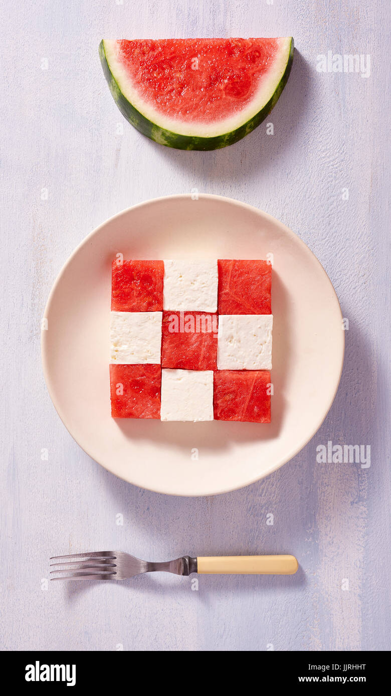 Würfel der Wassermelone und Feta Käse auf dem Teller zu einem quadratischen Muster mit Stück Melone und Gabel Stockfoto