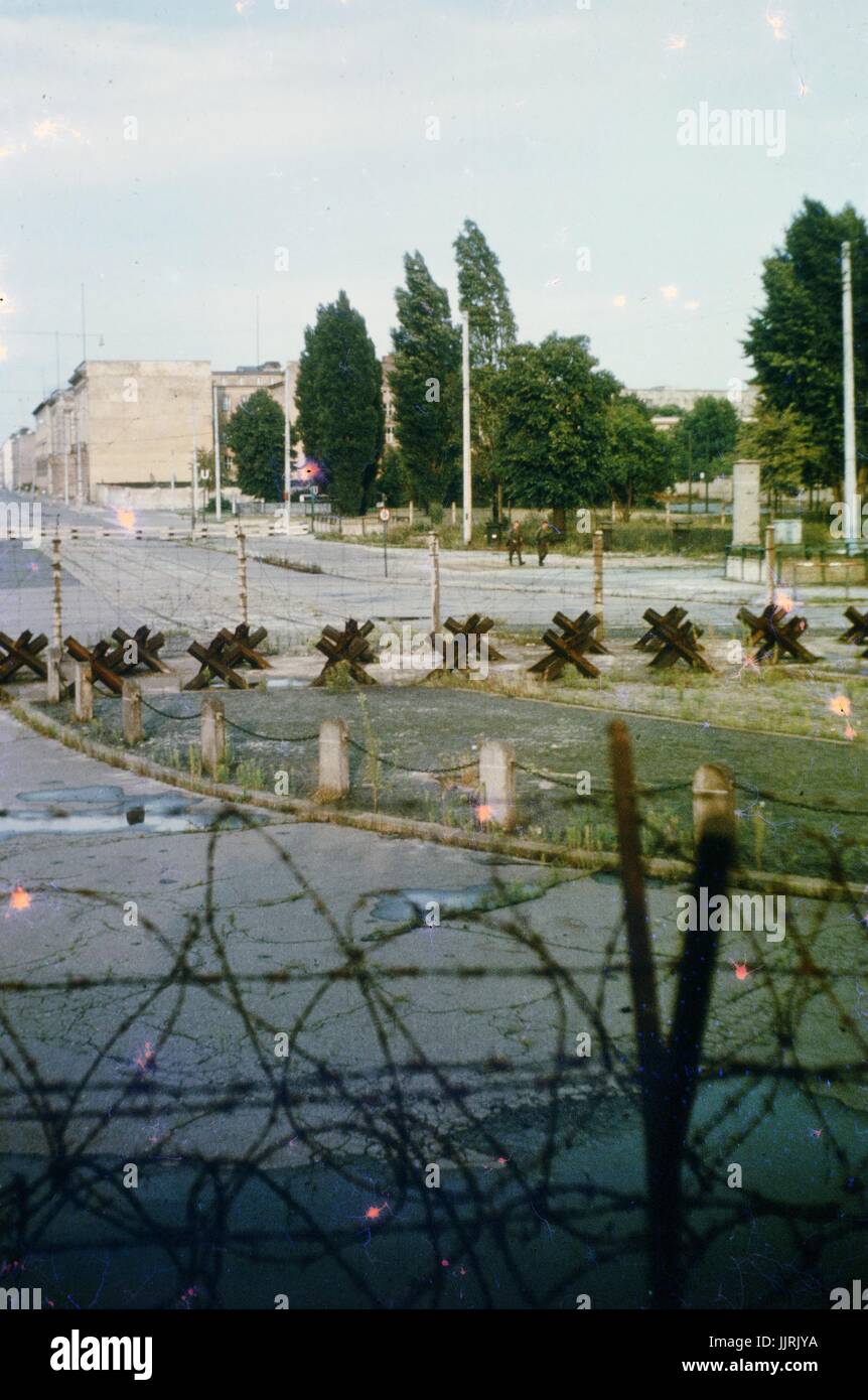 Blick durch Stacheldraht und Barrikaden über eine Grenze von West-Berlin nach Ost-Berlin während des Kalten Krieges, mit zwei Soldaten marschieren auf der Ost-Berliner Seite des Drahtes, Deutschland, 1970 zu sehen. Stockfoto