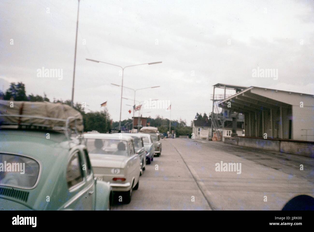 Eine Schlange von Autos wartet einen Checkpoint zwischen Ostberlin und West Berlin während des Kalten Krieges, mit Fahnen von Deutschland, den Vereinigten Staaten und sichtbar an der Vorderseite der Linie, Deutschland, Großbritannien 1970 zu überqueren. Stockfoto