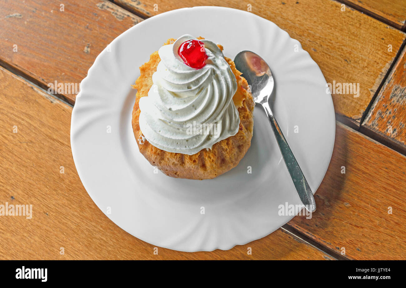 Savarin Kuchen mit Sahne und Sirup, Silberlöffel, weiße Platte auf Holz Hintergrund. Stockfoto