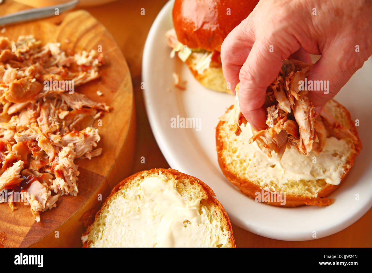 Ein Mann legt hausgemachte gezogen Huhn auf einem Brioche Brötchen Stockfoto