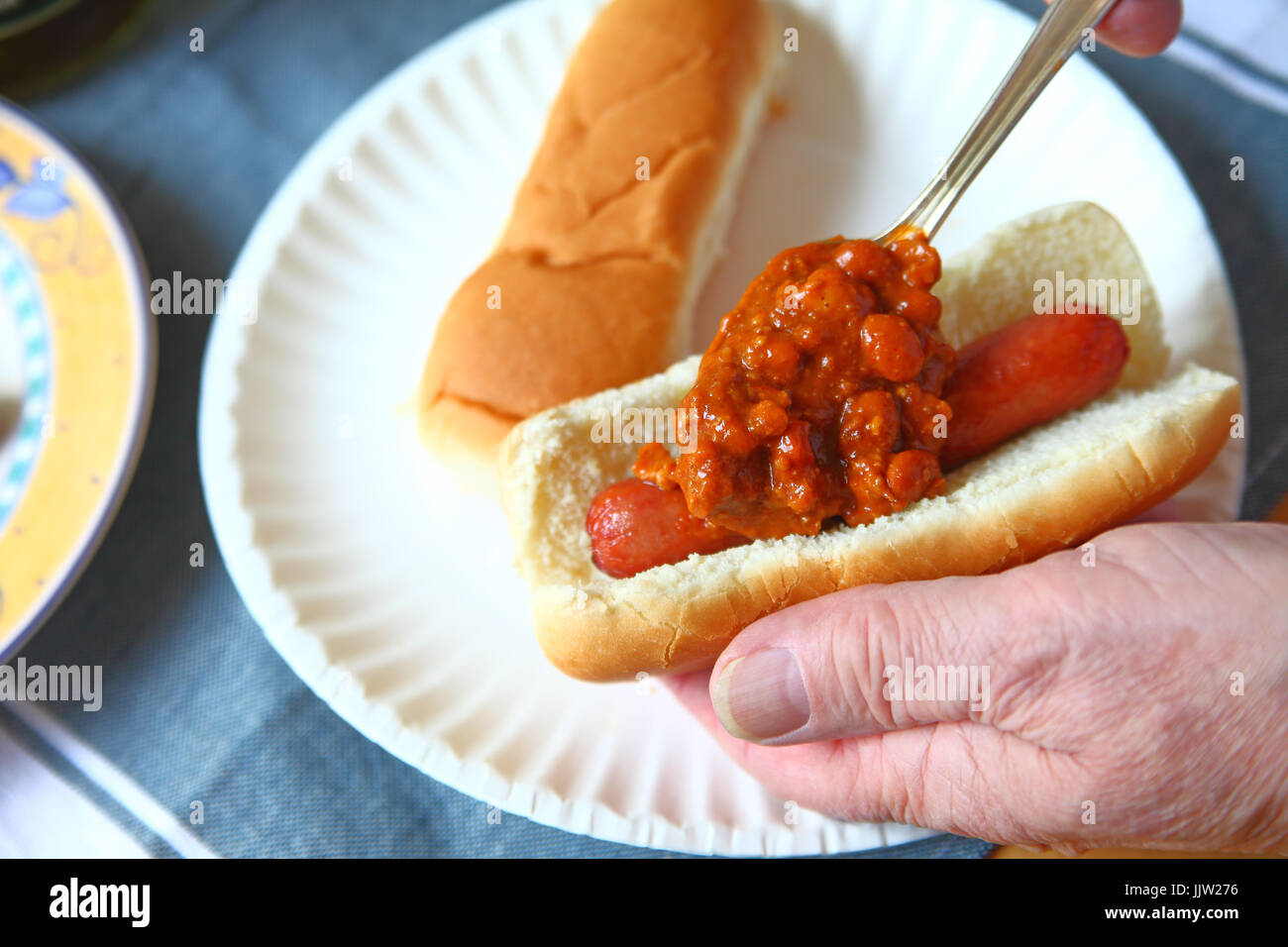 Ein Mann Löffel Chili mit Bohnen auf einen Hot dog über einem Papier Platte Stockfoto