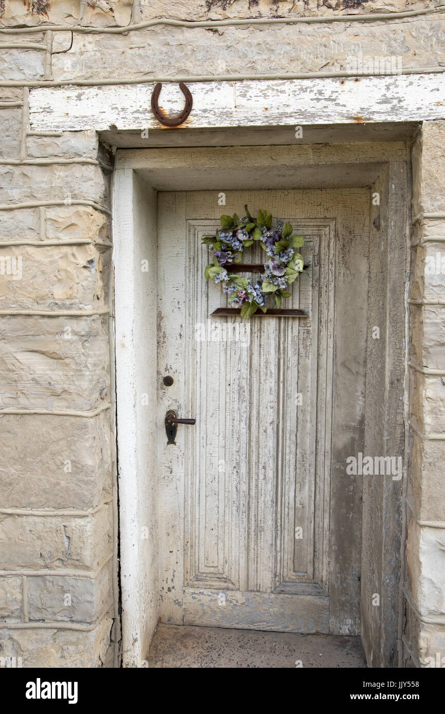 Blumengebinde auf Holztür in Steinmauer von rustikalen Altbau. Stockfoto
