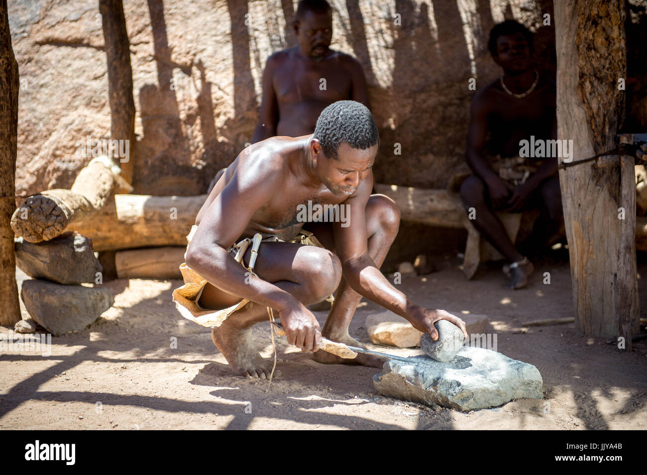 Ein Damara Mann nutzt Werkzeuge und Felsen zum Schärfen eines Messers im Damara Living Museum in Twyfelfontein, gelegen in der südlichen Region von Namibia, Afri Stockfoto