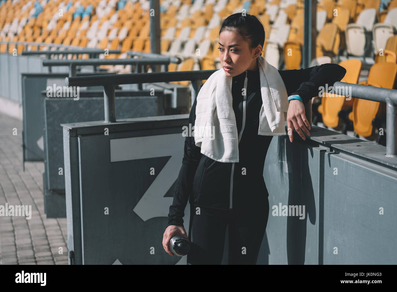 müde asiatischen Sportlerin ruht mit Sport-Flasche und Handtuch auf Stadion Stockfoto
