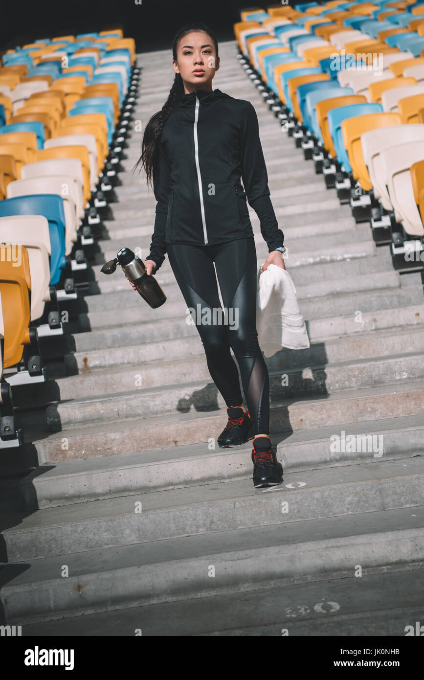 müde asiatischen Sportlerin mit Sport-Flasche und Handtuch auf Stadionsitze Stockfoto