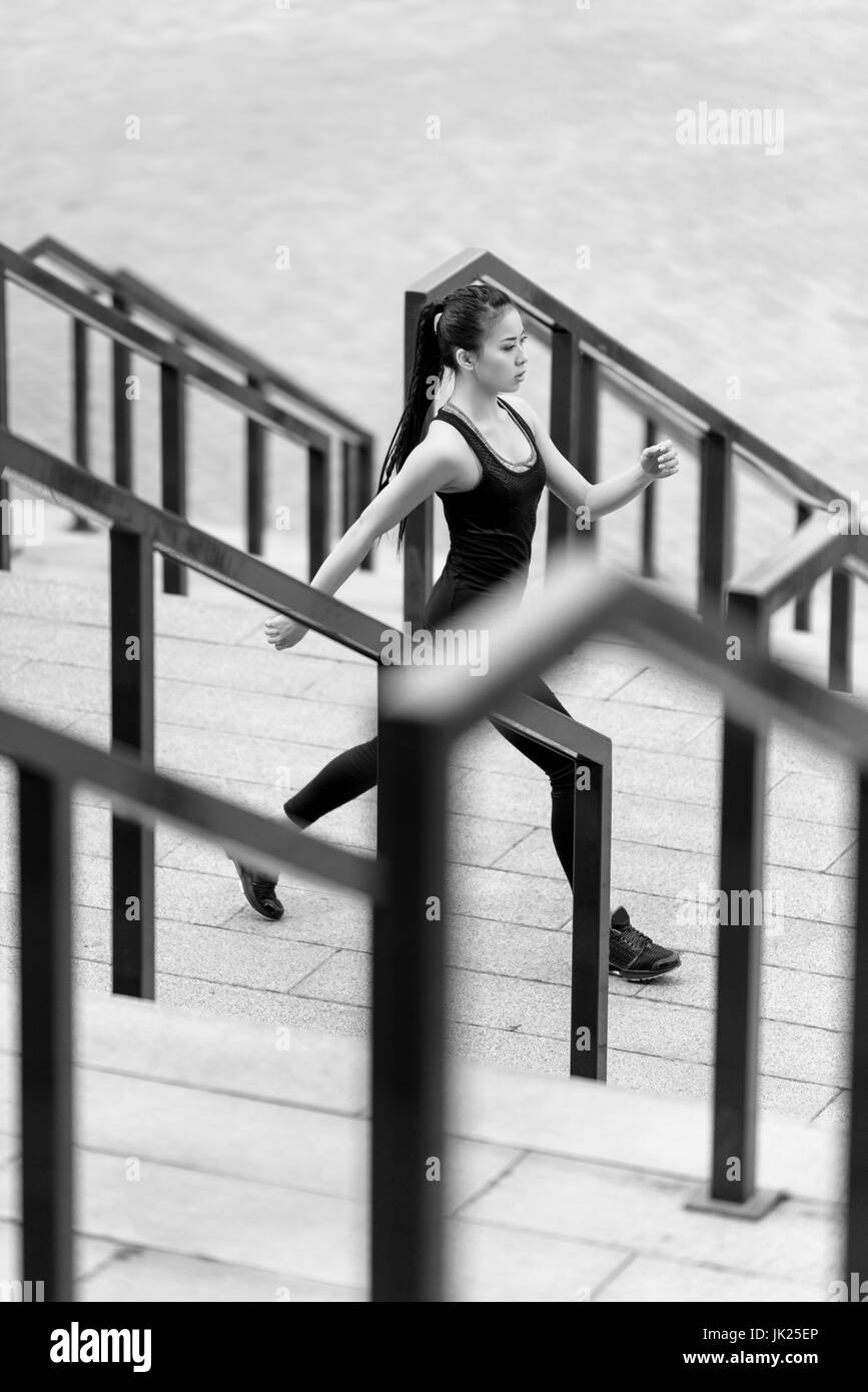 Junge sportliche Asiatin in Sportbekleidung Joggen am Stadion Treppe, schwarz / weiß Foto Stockfoto