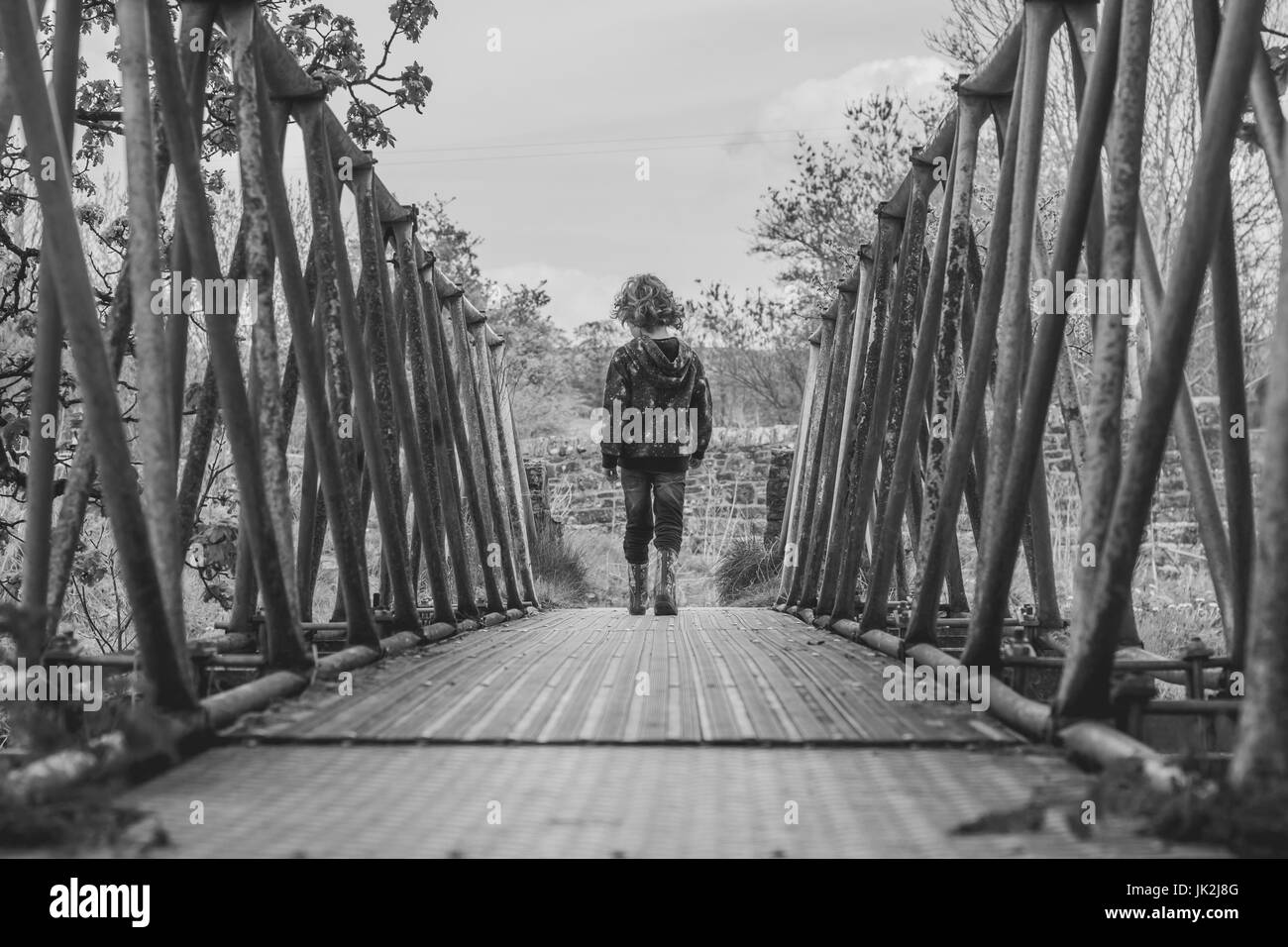 Schwarz / weiß Foto der Rückansicht eines kleinen Jungen auf einer Metallbrücke, genießen Sie einen Spaziergang auf dem Lande Stockfoto