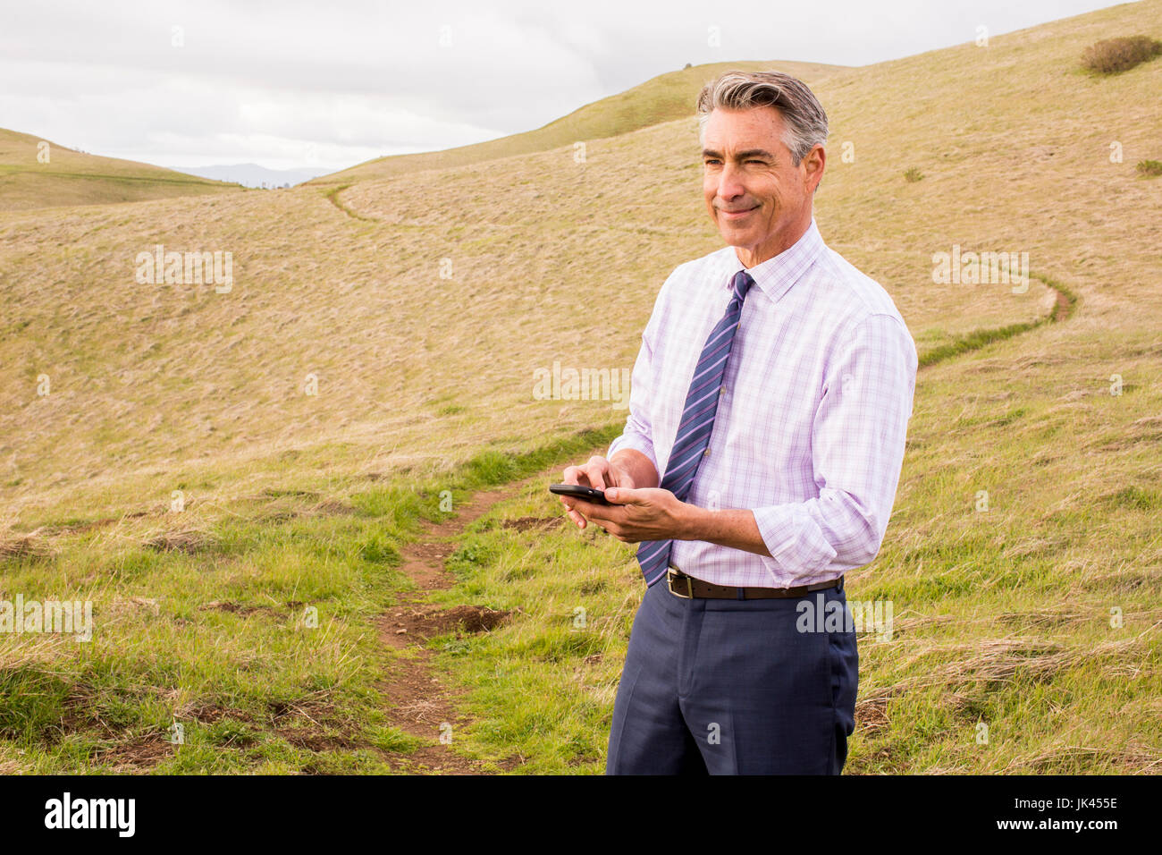 Lächelnd kaukasischen Geschäftsmann stehend Gras hält Handy Stockfoto