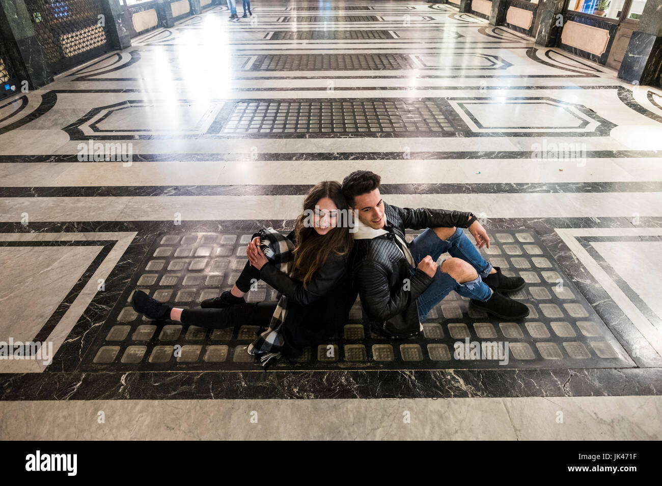 Kaukasische paar sitzen Rücken an Rücken am Boden der lobby Stockfoto