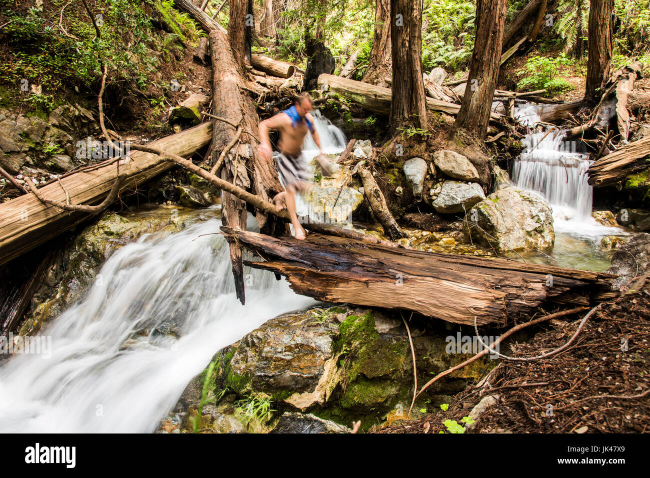 Kaukasischen Mann zu Fuß über Wasserfall auf Log in Wäldern Stockfoto
