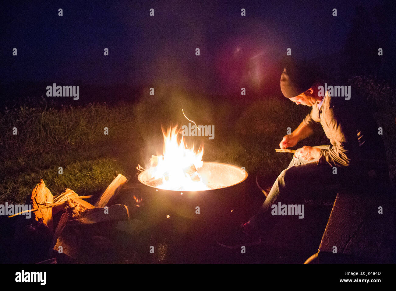 Kaukasischen Mann Schnitzen von Holz in der Nähe von Lagerfeuer am Abend Stockfoto