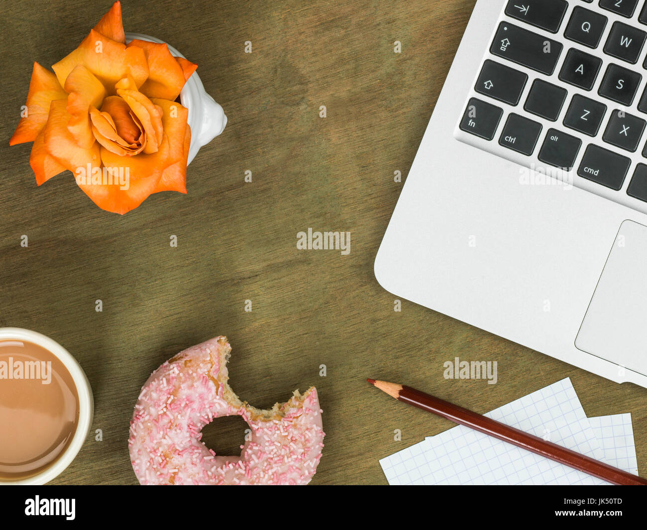 Eistee Donut an einen Computer-Arbeitsplatz mit einer Tasse Tee gegen eine notleidende Schreibtisch aus Holz Stockfoto