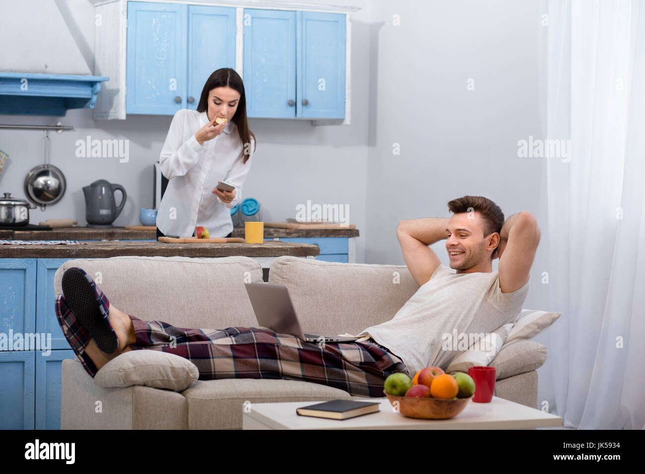 Mann auf Sofa liegend, während seine Frau vorbereitet ist, zur Arbeit zu gehen. Stockfoto