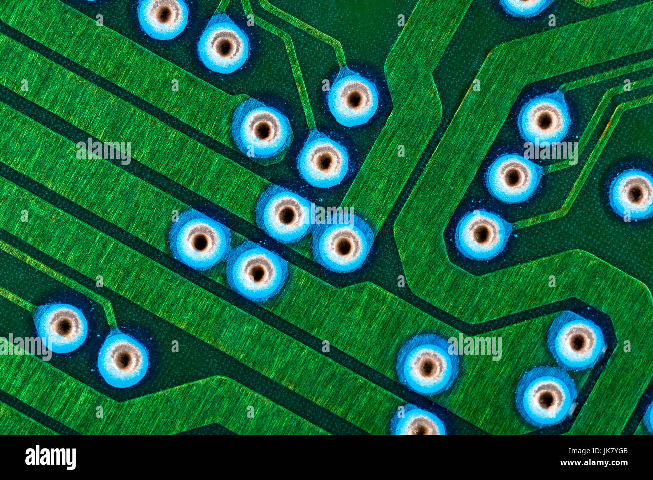 Makrofoto der Anschlussspuren auf grüner Leiterplatte (pcb) mit blauen Tauchlöchern sichtbar. Verkabelung im Computer, Details zum Schließen des Stromkreises. Stockfoto