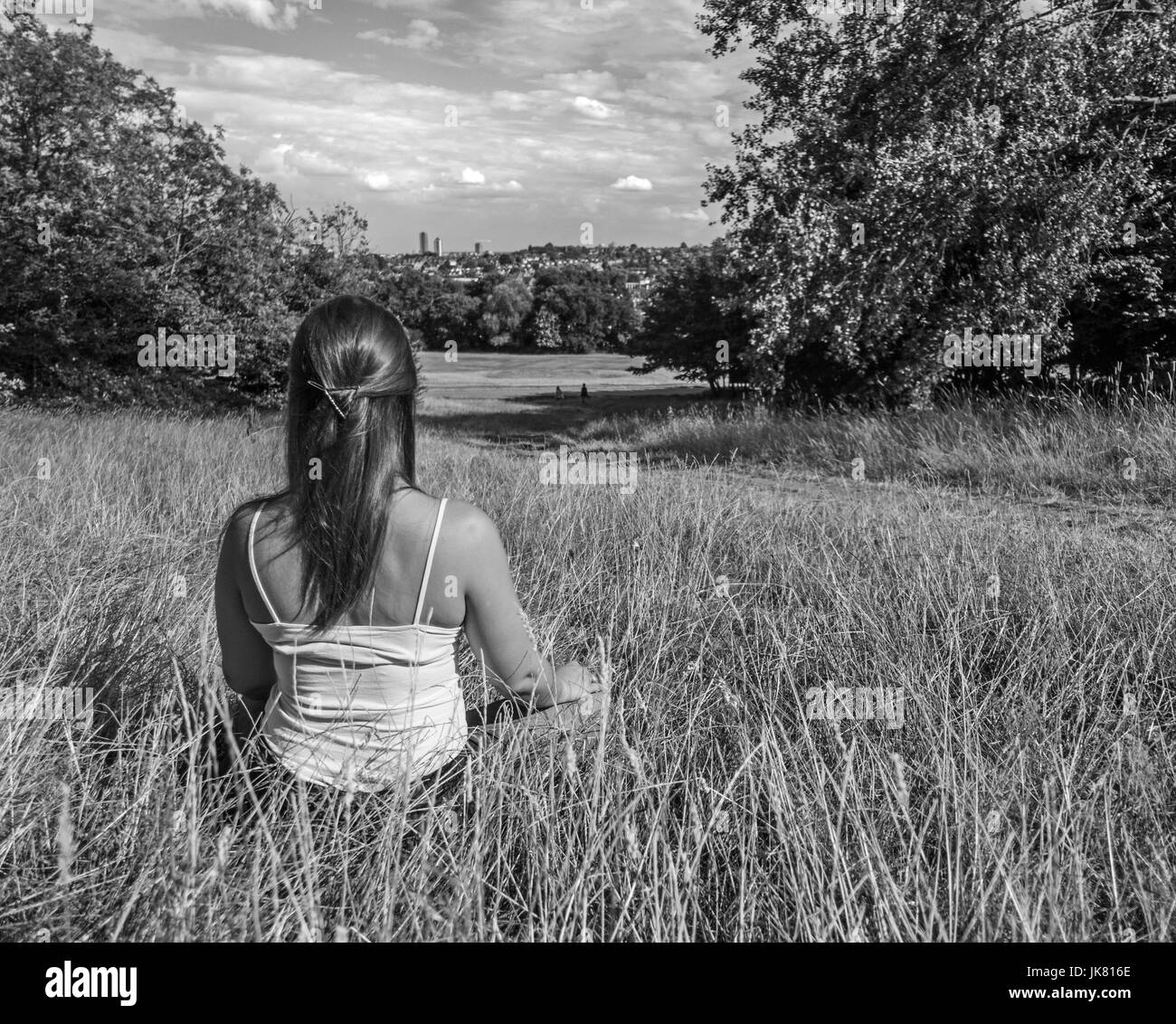Junge Frau sitzend meditierend in Rasen mit Blick auf eine Stadt Stockfoto