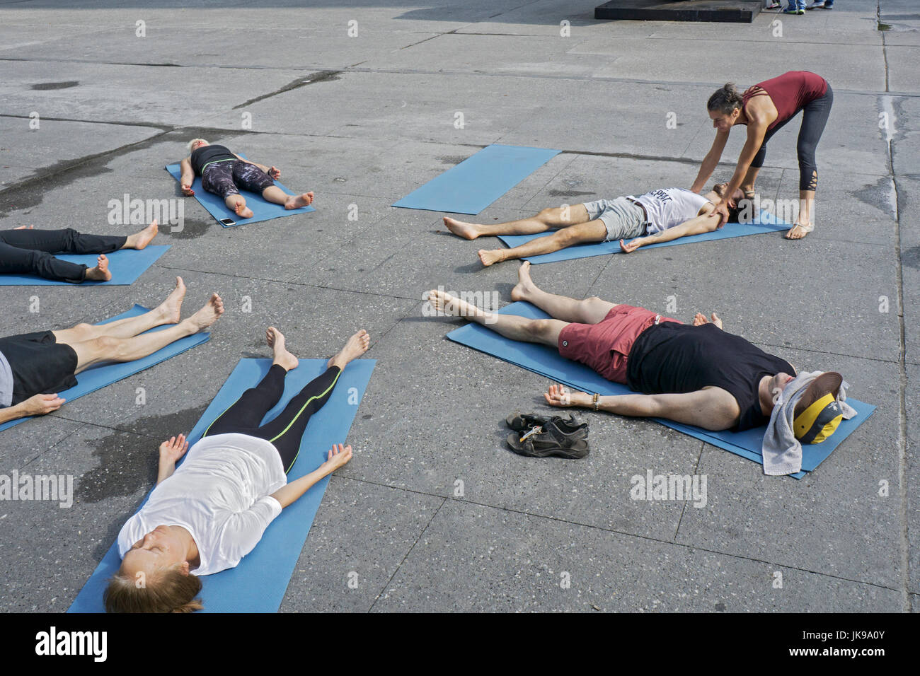 Um eine kostenlose Yogastunde auf Astor Place in Greenwich Village passt der Kursleiter eines Schülers Position. Stockfoto