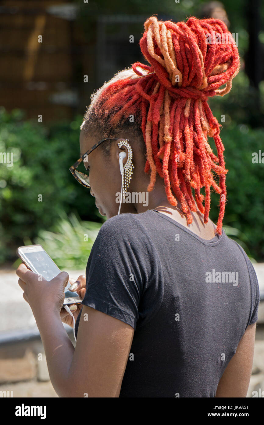 Eine junge Frau mit orange und Magenta Haarverlängerungen und eine aufwendige Ohrring-SMS auf ihr Handy in Manhattan, New York City. Stockfoto