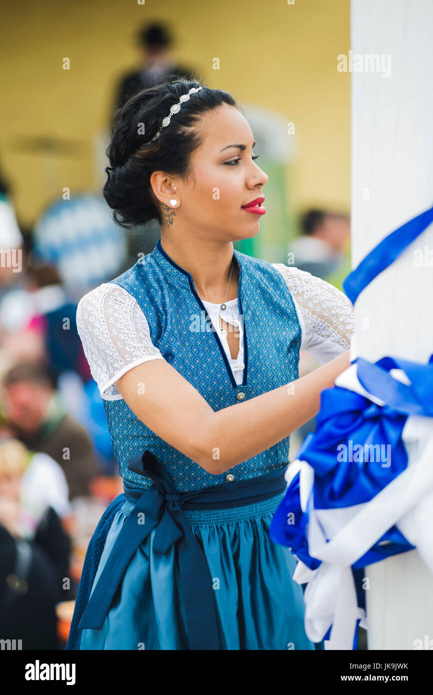 Junge Bayerin im traditionellen Dirndl Kleid verknoten ein blaues Band um den Maibaum vor der Durchführung des traditionellen Volkstanz Bandltanz Stockfoto