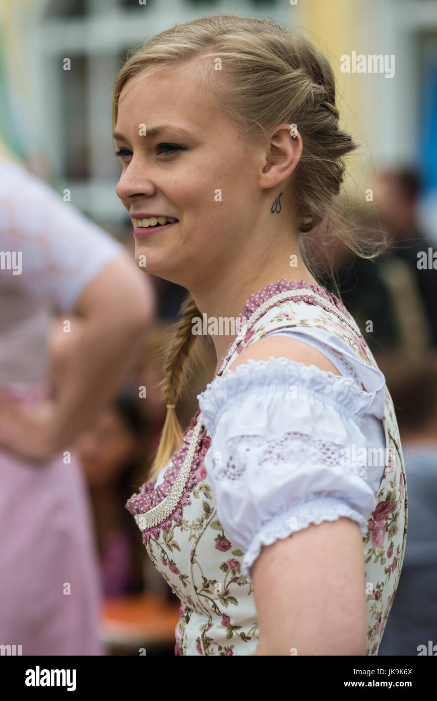 Junge Bayerin im traditionellen Dirndl Kleid mit Armen gestemmt suchen beiseite während der Durchführung traditionellen Volkstanz Bandltanz rund um den Maibaum Stockfoto
