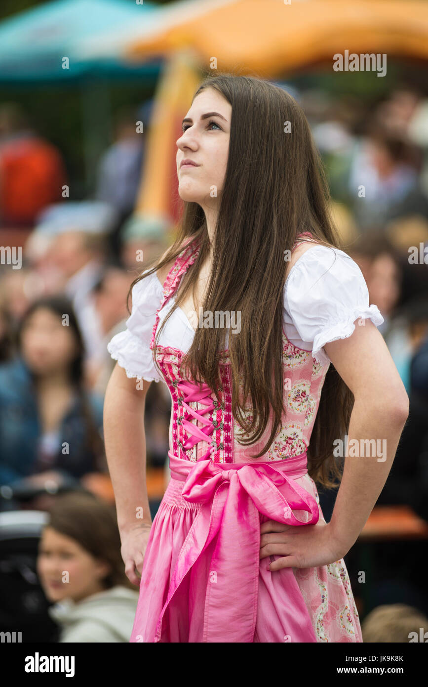 Junge Bayerin im traditionellen Dirndl Kleid mit Armen gestemmt nachschlagen während der Durchführung traditionellen Volkstanz Bandltanz rund um den Maibaum Stockfoto