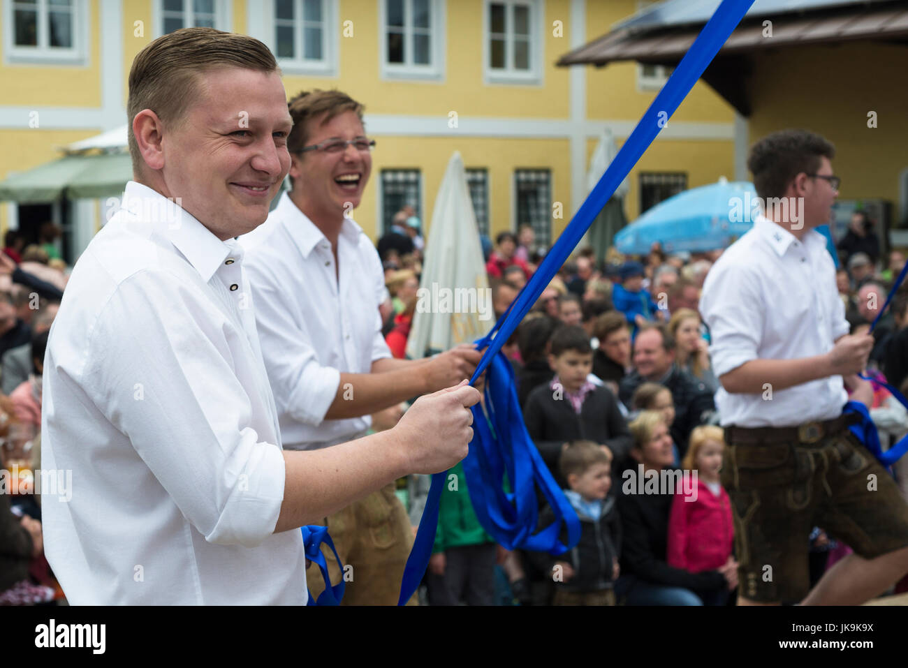 Junge bayerische Männer in weißen Hemd und Lederhose hält blaues Band während der Durchführung traditionellen Volkstanz Bandltanz rund um den Maibaum Stockfoto
