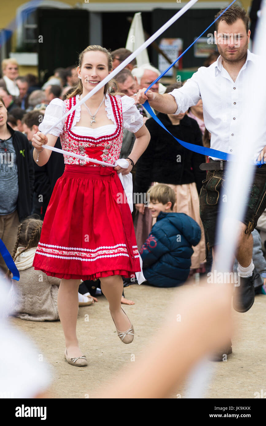 Junge Bayerin im traditionellen Dirndl Kleid Holding blaues Band während der Durchführung traditionellen Volkstanz Bandltanz rund um den Maibaum Stockfoto