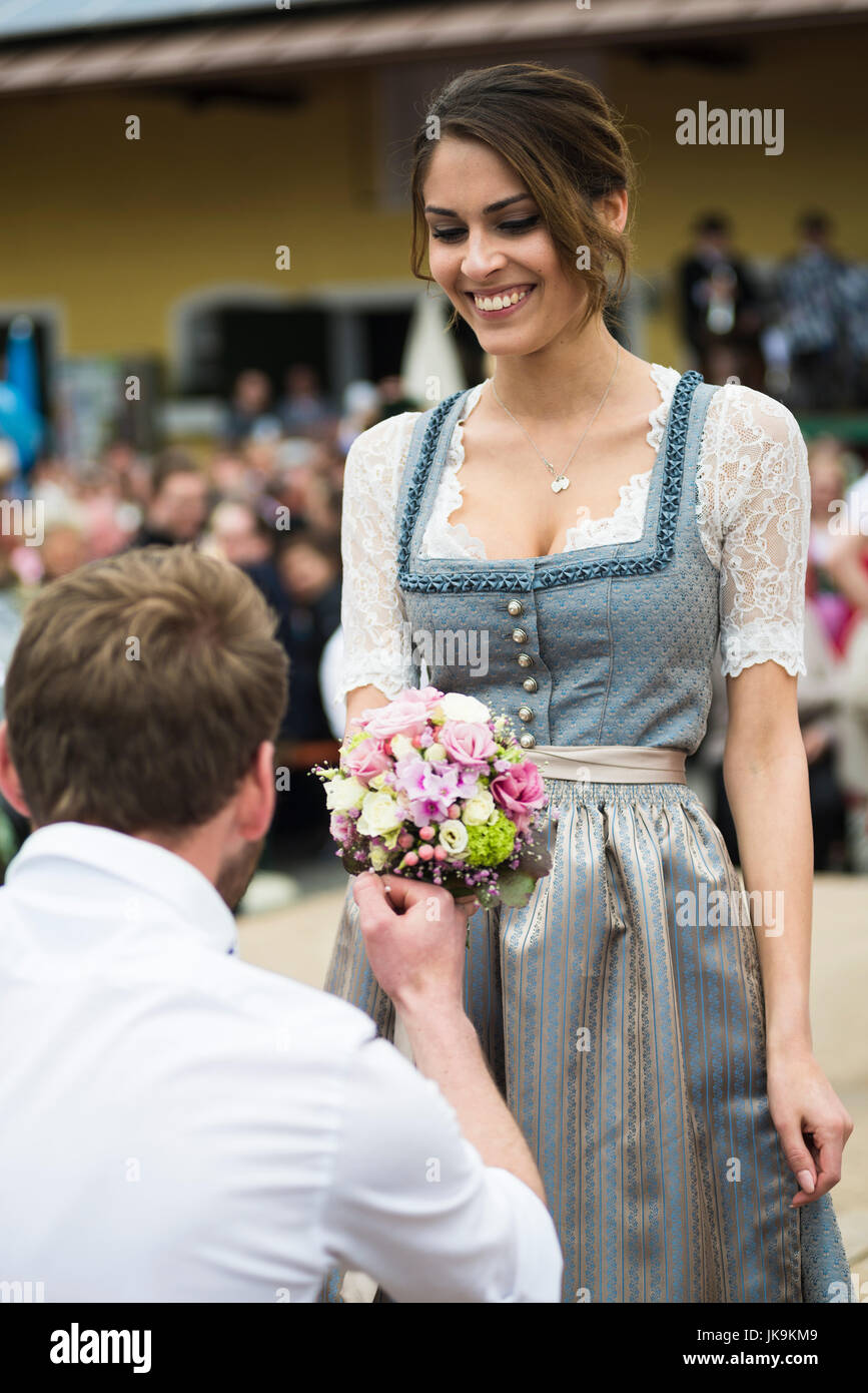 Porträt eines jungen Mannes, kniend vor einer Frau mit einem Bouquet von Blumen, die Durchführung eines traditionellen bayerischen Volkstanzes Bandltanz um einen Maibaum Stockfoto