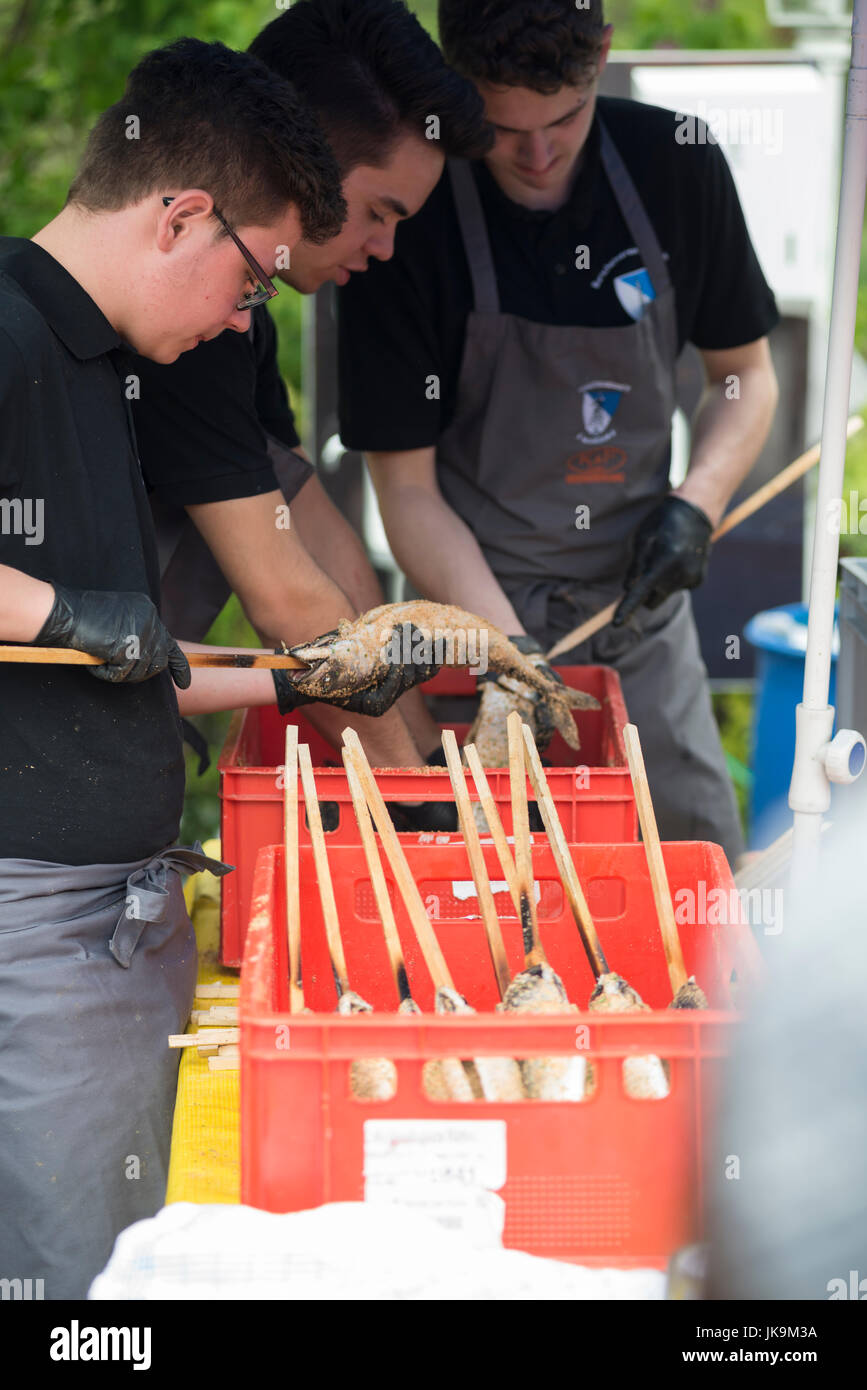 Panierter Fisch sind auf einem Holzstab von jungen Männern, zum Grillen als einheimische Spezialität in Bayern auf Mai Feier spucken Stockfoto