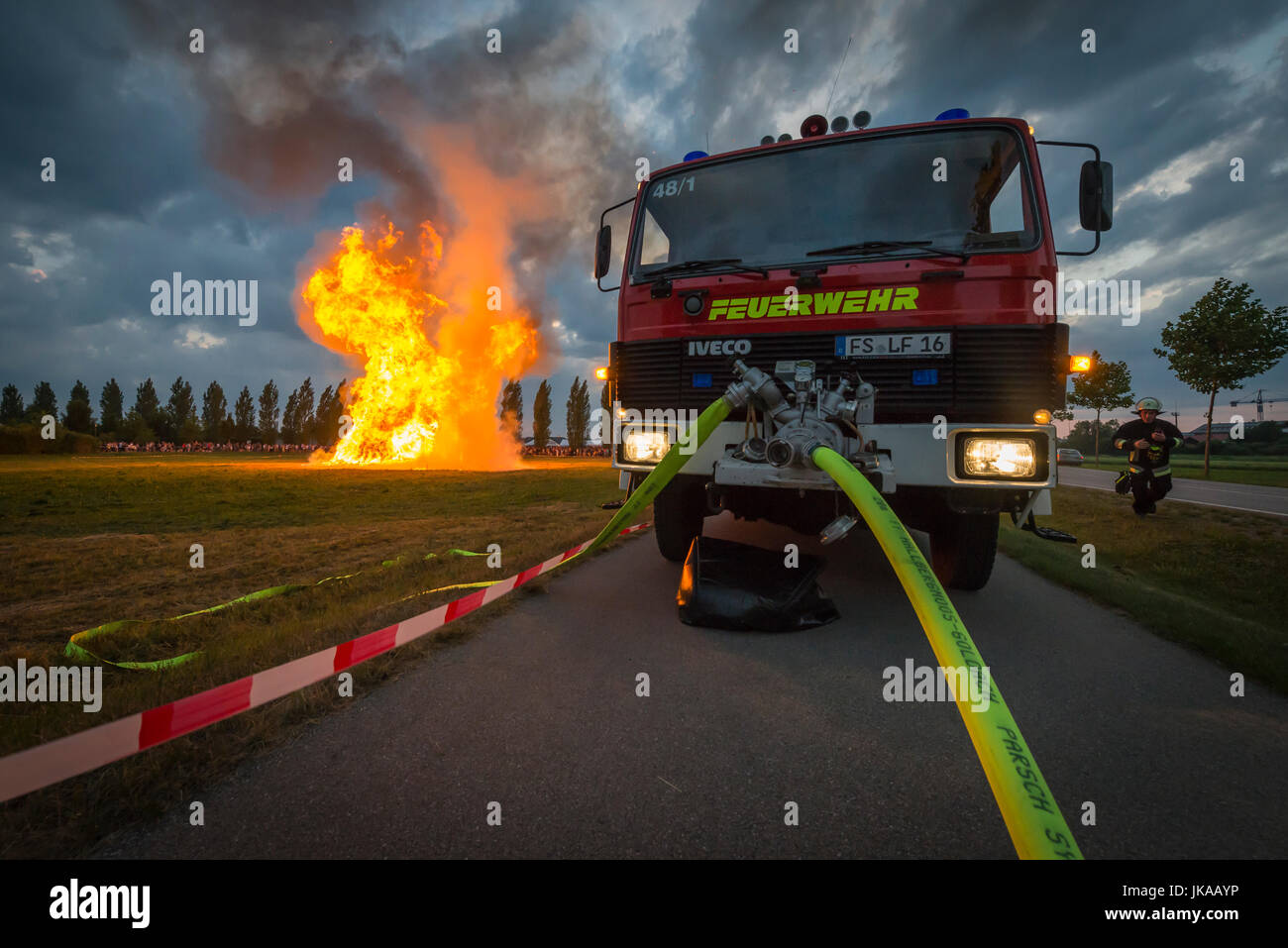 Fire-Fighter auf Feuerwehrauto spritzt Wasser gegen Funkenflug der Feuersäule bei Sonnenwende feiern und Sonnwendfeuer Stockfoto